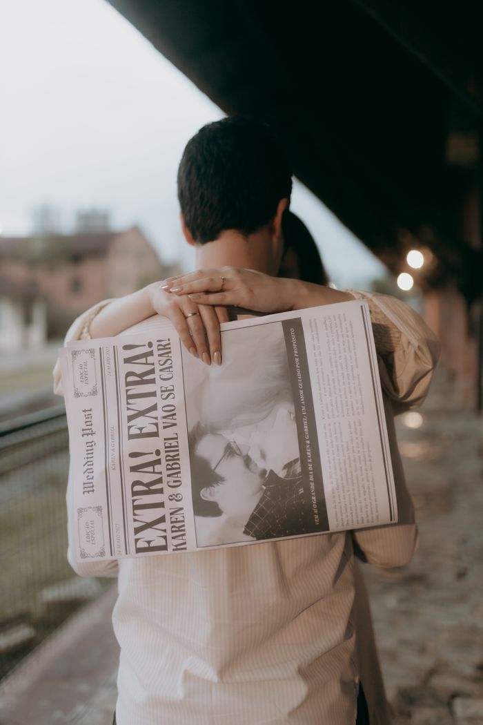 Couple embraces while holding a newspaper with a wedding ad at a train station.