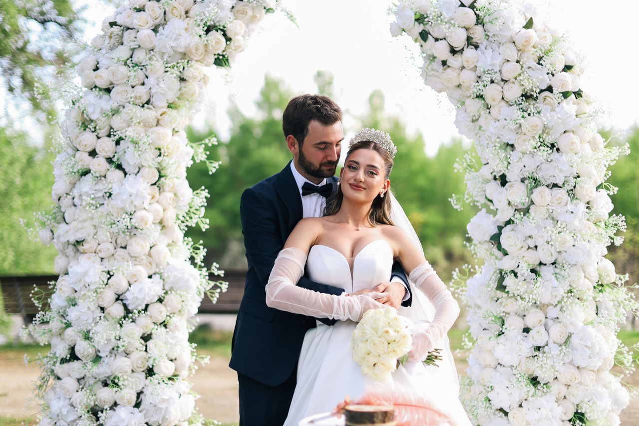 Beautiful outdoor wedding with a couple under a floral arch, captured in natural light.
